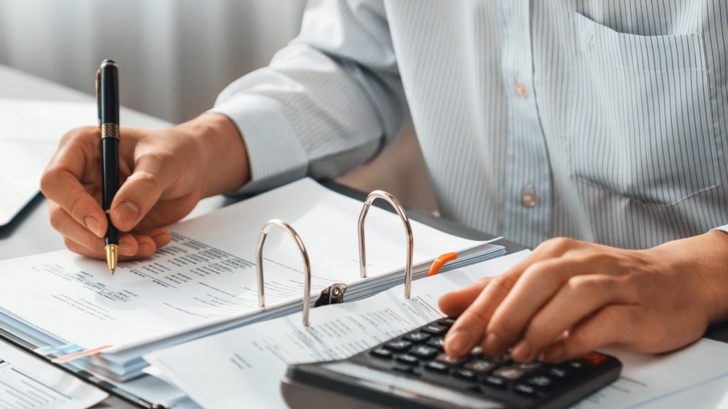 Corporate auditor calculating budget with calculator on his office desk. Insight